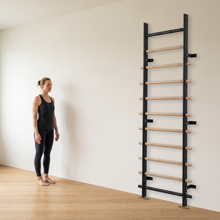 TWHEELS Sprossenwand Standard mit sichtbarem Wandabstand in einem hellen Trainingsraum neben einer Sportlerin.