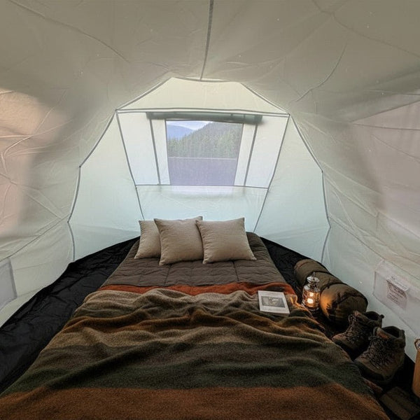 Blick in die Schlafkabine mit gemachtem Bett, Kissen, Decken und Laterne in gedämpftem Abendlicht